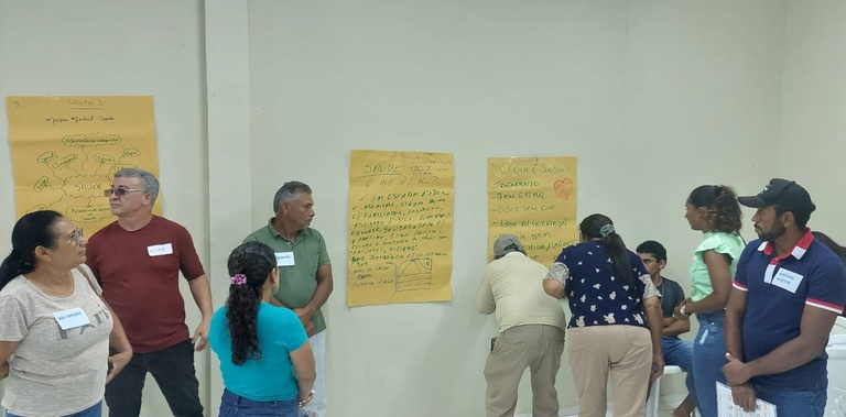Participantes com crachás de identificação interagem em grupo diante de cartazes manuscritos e mapas mentais colados na parede.