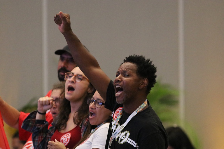 Um homem negro com o punho erguido e expressão de clamor representa a forte participação social na conferência.