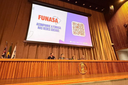 Homem palestra em palco com painel "Arena do Conhecimento" e tela ao fundo sobre saneamento no FISA 2026.