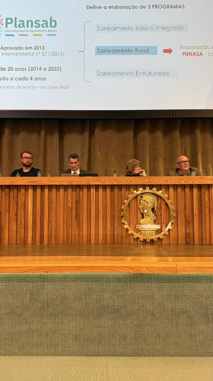 Palestra em auditório com telão ao fundo exibindo informações sobre o Programa Nacional de Saneamento Rural (PNSR).