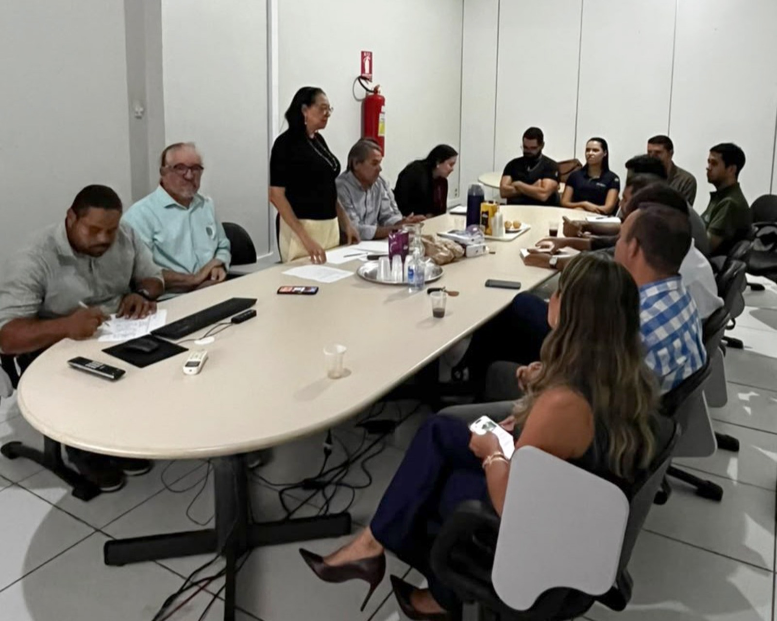 Grupo de pessoas reunido ao redor de uma grande mesa oval em sala de reuniões.