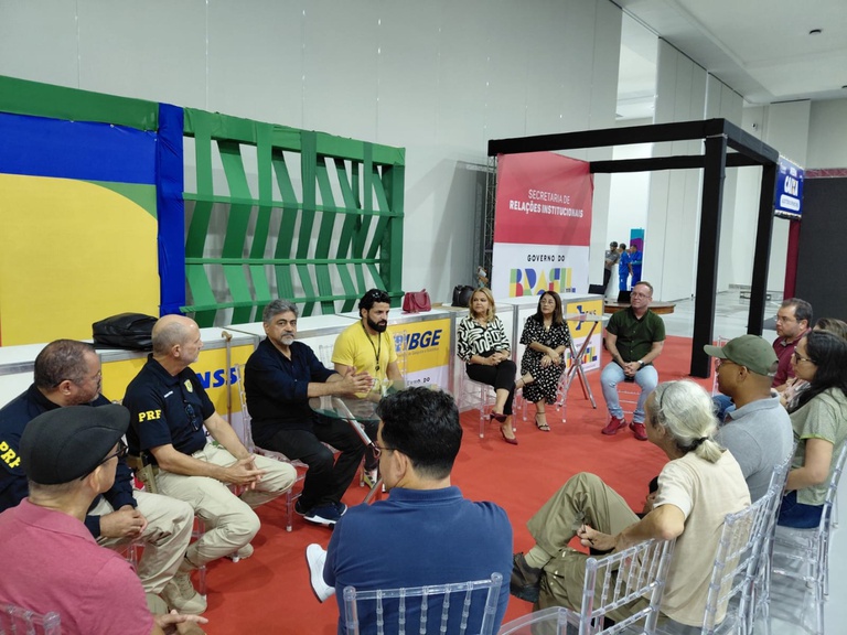 Reunião em círculo com representantes de órgãos federais, como PRF e IBGE, em espaço de eventos com tapete vermelho.