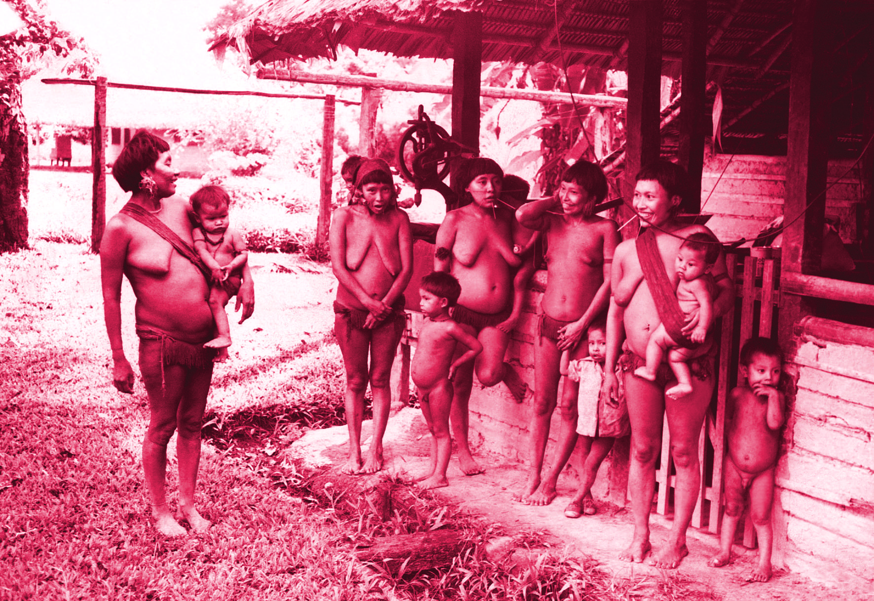 Grupo de indígenas reunidos em frente a uma habitação de palha, com efeito visual avermelhado.