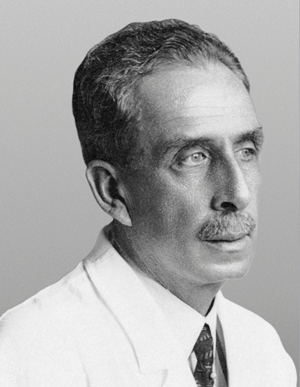 Retrato em preto e branco de Carlos Chagas de perfil, vestindo jaleco branco e gravata.