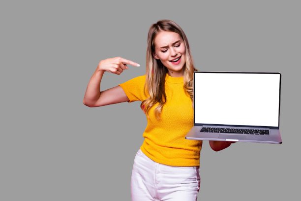 Foto de mulher jovem sorridente, em uma parede cinza apontando para tela do computador Laptop