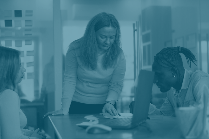 Duas mulheres e um homem sentados ao redor de uma mesa, com um notebook, discutindo estratégia.