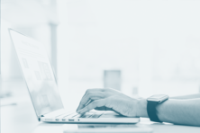 Notebook aberto, mão de uma pessoa digitando no notebook.