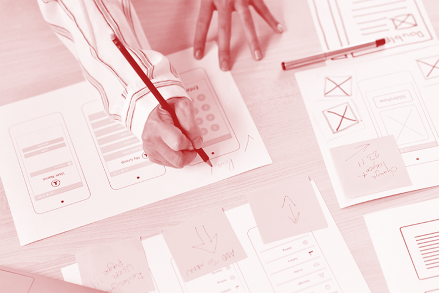 Mão de uma pessoa desenhando em uma folha com imagem de um celular.