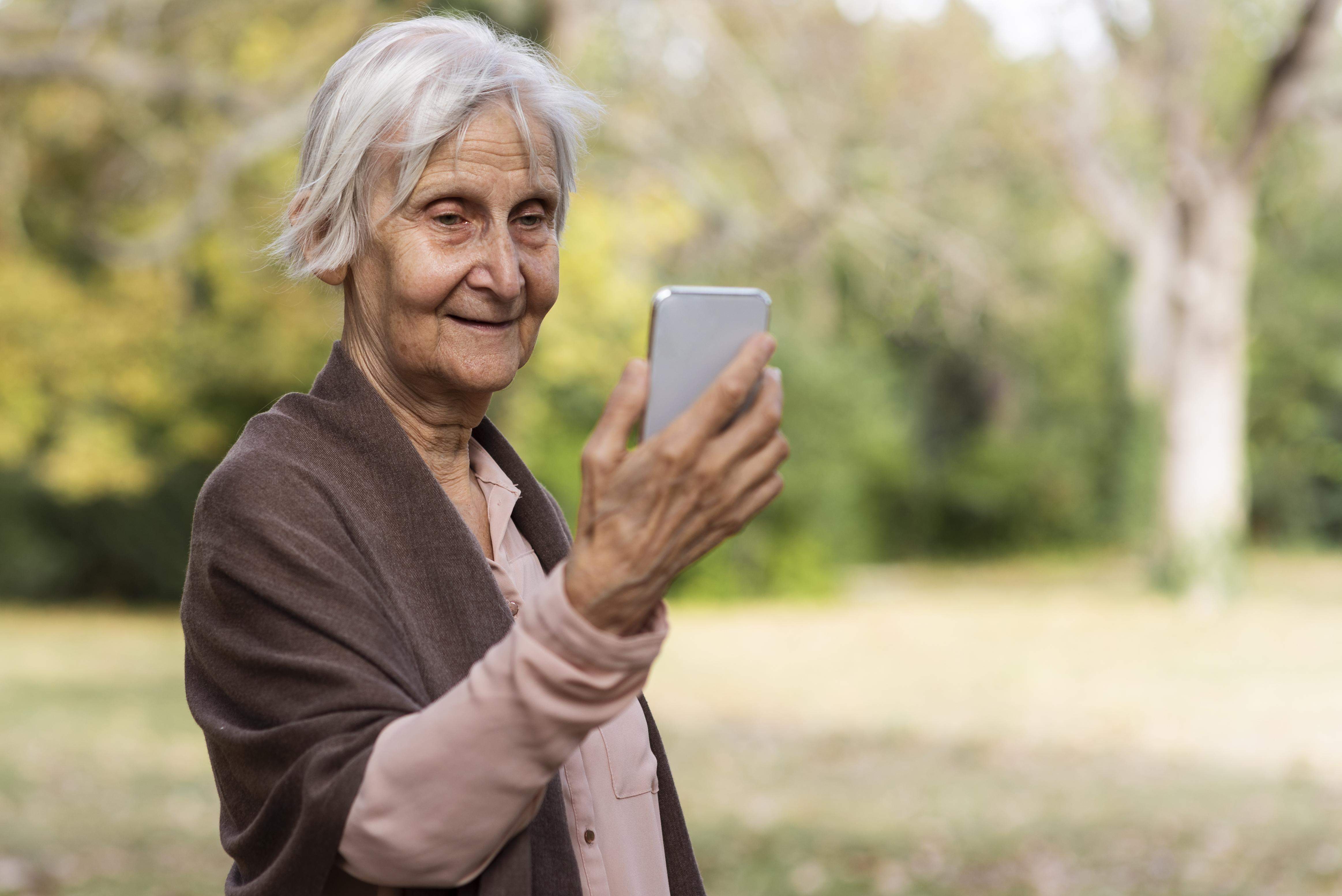Mulher mais velha sorridente segurando smartphone e ao ar livre