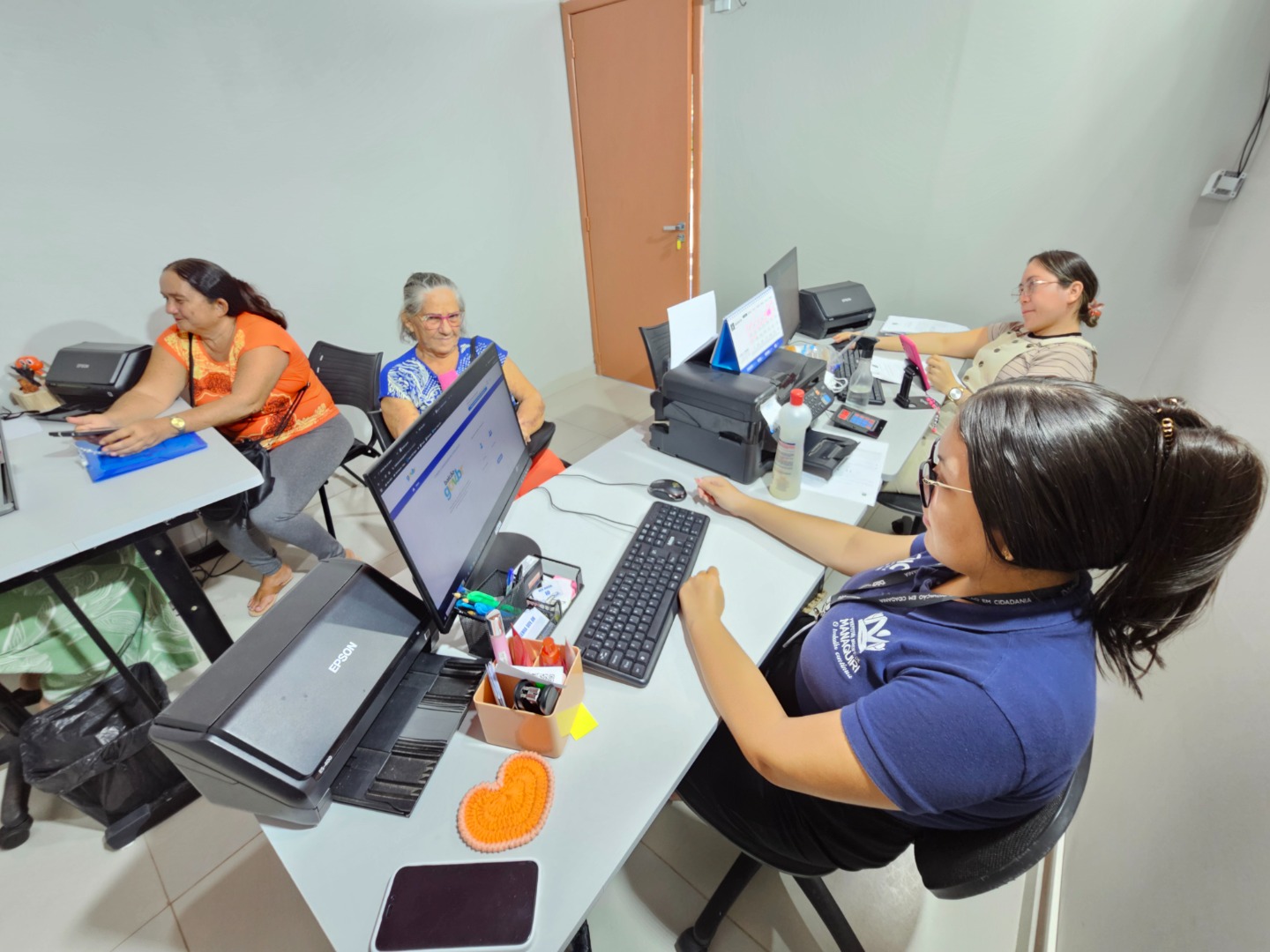 Funcionários do Centro de Tecnologia e Inovação Em Cidadania (CTIC) em Manaquiri, Amazonas, orientando cidadãos em balcões de atendimento, com serviços públicos sendo realizados presencialmente.