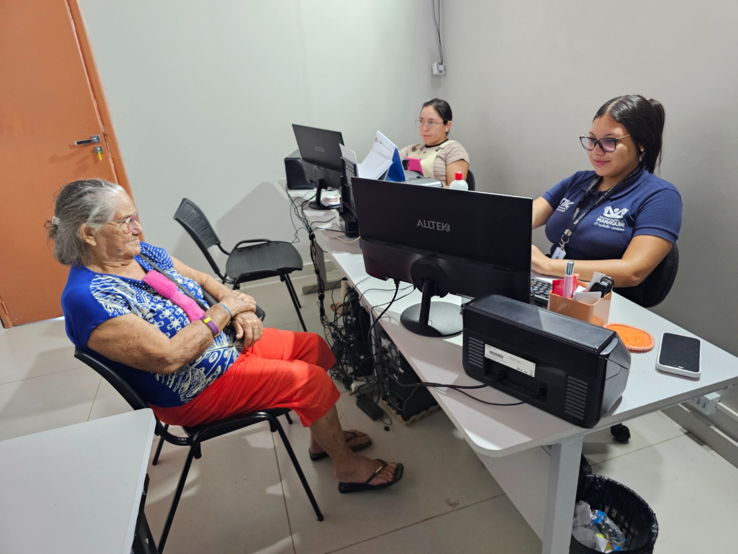 Atendimento presencial no Centro de Tecnologia e Inovação Em Cidadania (CTIC) em Manaquiri, Amazonas, com funcionários auxiliando cidadãos em um ambiente organizado de serviços públicos.
