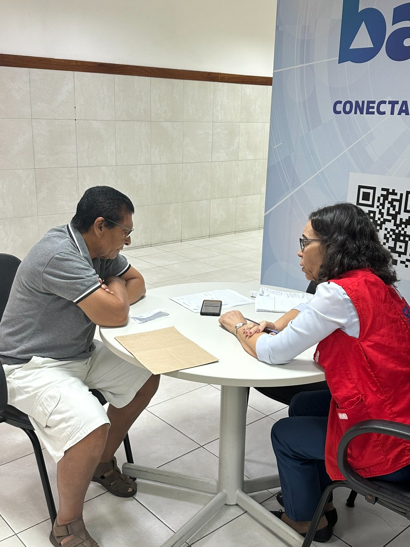 Ambiente de atendimento do SAC da Bahia, com pessoas recebendo orientação presencial de servidores em guichês organizados.