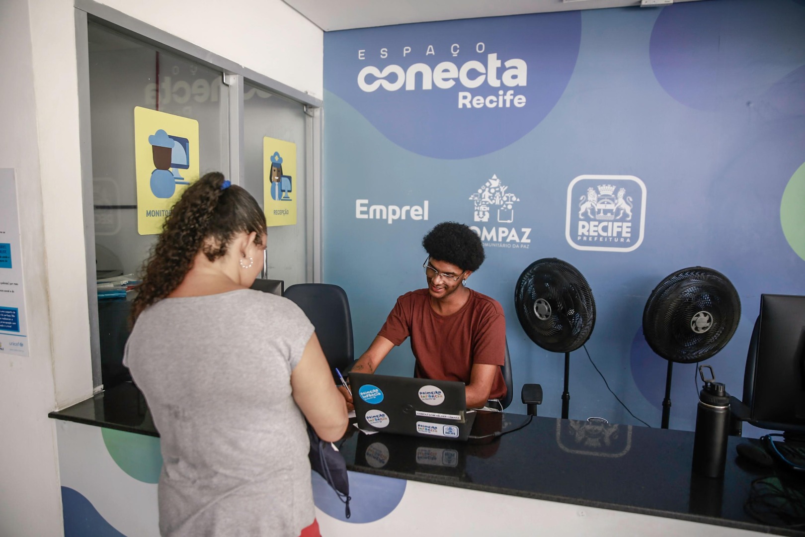 Atendentes do Expresso Cidadão no Recife auxiliando moradores em serviços presenciais, com ambiente amplo e organizado.