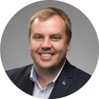 Foto de frente, da cintura para cima, de Siim. Homem jovem, que possui cabelos claros, veste terno escuro, camisa branca com estampas pequenas, sem gravata