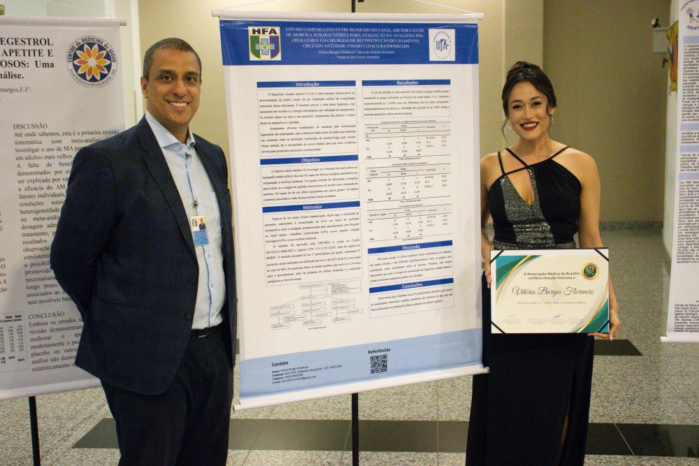 1º Ten QOMed Aer Albertino e a Dra Vitória Borges e o ao lado do Banner, cujo o trabalho intitulado foi “Estudo comparativo entre o bloqueio do canal dos adutores e o uso de morfina subaracnóidea para analgesia em cirurgias de reconstrução ligamentar do joelho: Estudo clínico randomizado”