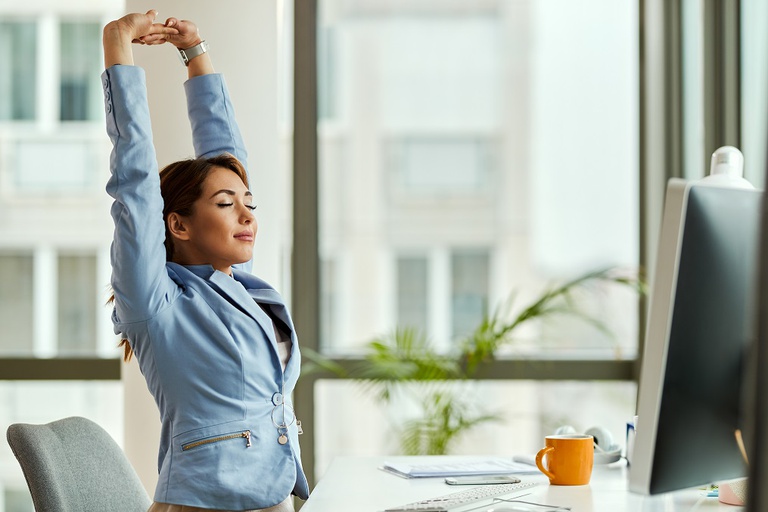 young-smiling-businesswoman-stretching-with-her-eyes-closed-while-working-on-a-computer-in-the-office.jpg