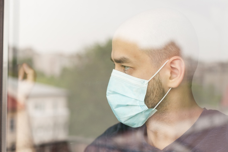 unhappy-man-looking-through-window-wearing-protection-mask-self-isolation.jpg