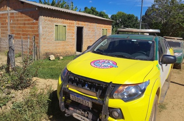 Uma caminhonete amarela do Prevfogo e uma caminhonete verde do Ibama estão estacionadas em frente a uma casa de tijolos e janelas venezianas amarelas em uma zona rural de Goiás. Entre as janelas, há uma porta aberta. Ao lado da casa, há um terreno baldio com uma cerca rudimentar. 