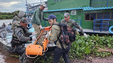Felino é transportado no suporte de cor laranja pela equipe envolvida na captura e na realocação do animal, que utiliza uma lancha para transportar o animal.