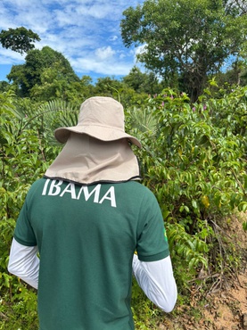 servidor do Ibama está de chapéu, em uma área de mata. À sua frente está uma vegetação mais baixa e, ao fundo, aparecem algumas árvores mais altas.