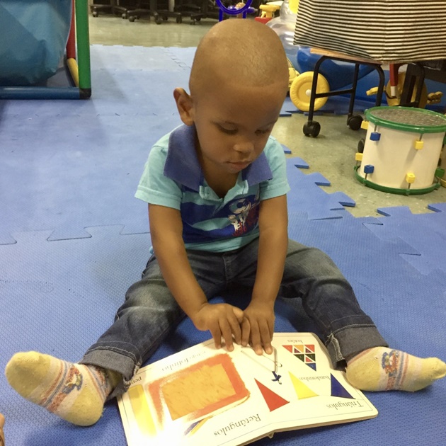Menino sentado no chão toca num livro tátil