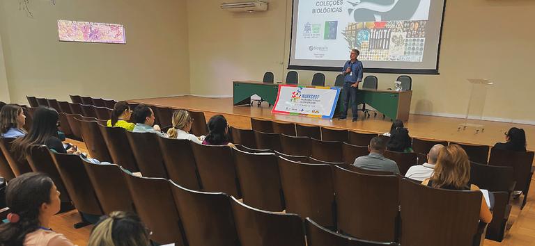 Auditório com homem branco discursando ao fundo