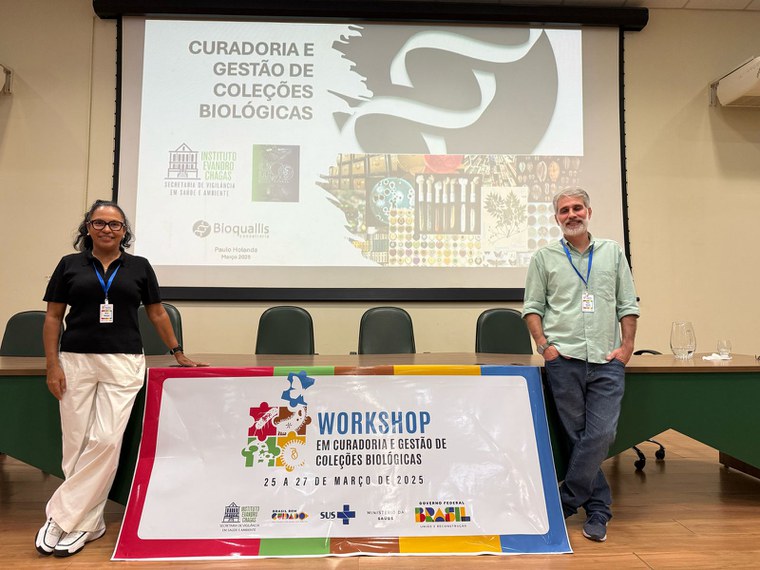 Silvia Marques e Paulo Holanda em frente ao banner do evento