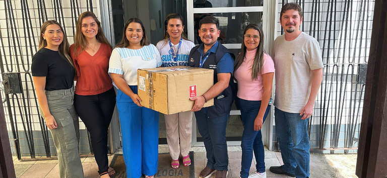 Equipe reunida para entrega de materiais na entrada de setor com caixa identificada como frágil.