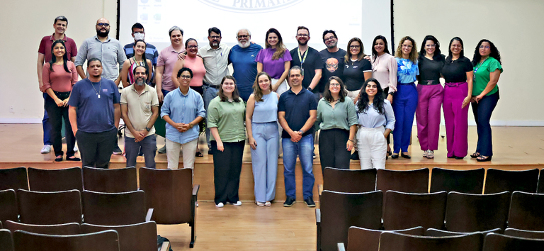 Grupo de pessoas sorrindo em um auditório, posando para foto coletiva sobre o palco.