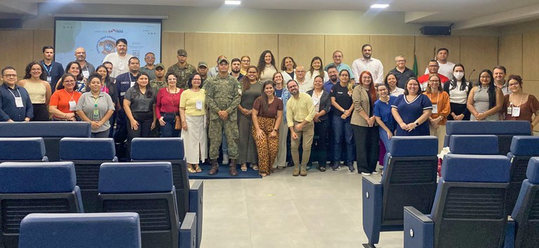 Grupo diverso de pessoas posa sorrindo em auditório, em frente a telão com logomarca da COP30.