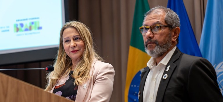 Ethel Maciel e Rivaldo Venâncio falam em evento, com bandeiras do Brasil e ONU ao fundo.