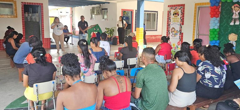 Pessoas assistem a palestra sobre saúde em espaço escolar decorado com cartazes e balões coloridos.