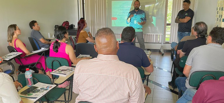 Sala de aula com pessoas sentadas assistindo à apresentação de homem em frente ao projetor