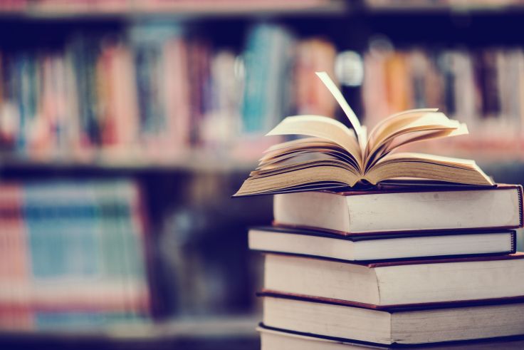 livros-abertos-sobre-mesa-e-estante-com-livros-desfocados-atras