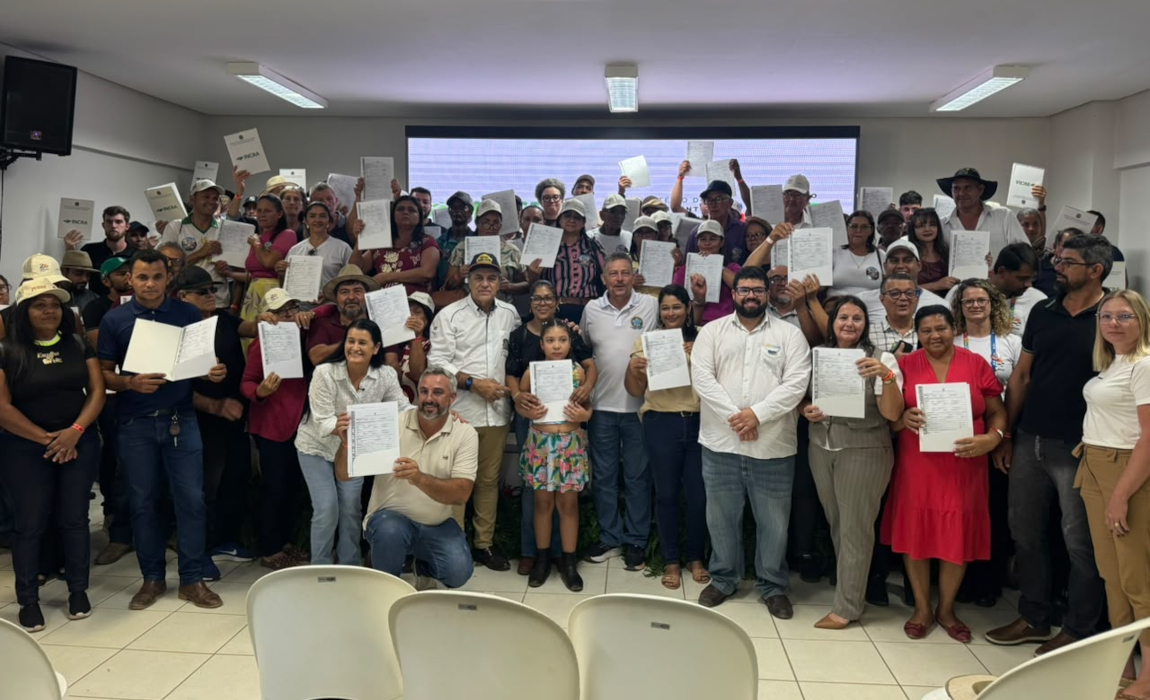 Homens e mulheres em pé, alguns segurando documentos, em clima de comemoração.