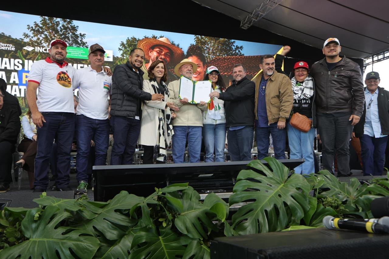 Presidente Lula em palco com várias pessoas entregado documentos