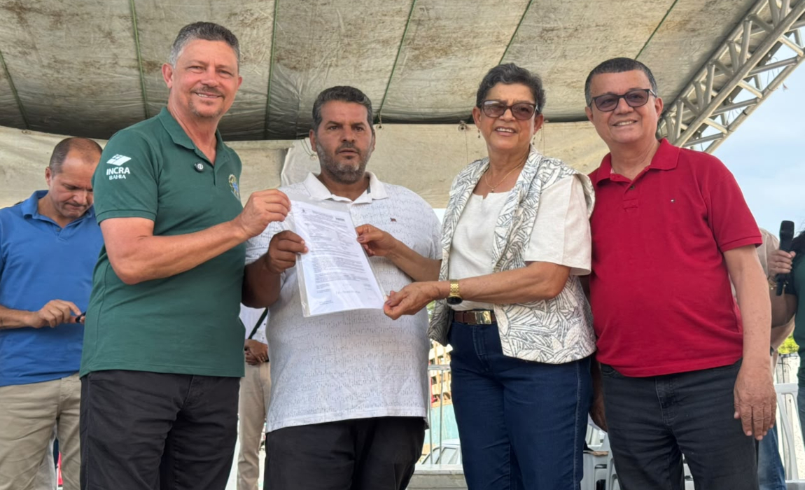 Três homens e uma mulher em pé em clima de comemoração com um dos homens segurando um documento.