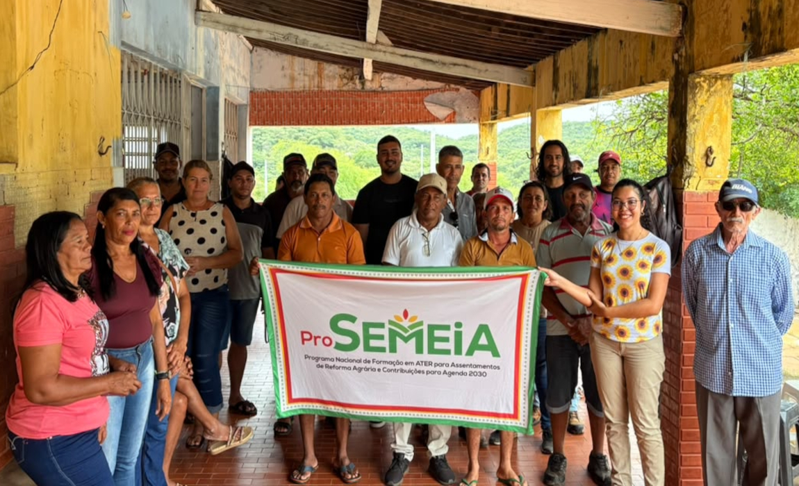 Homens e mulheres em pé, segurando um cartaz com o nome Pro-Semeia, na varanda de uma casa.