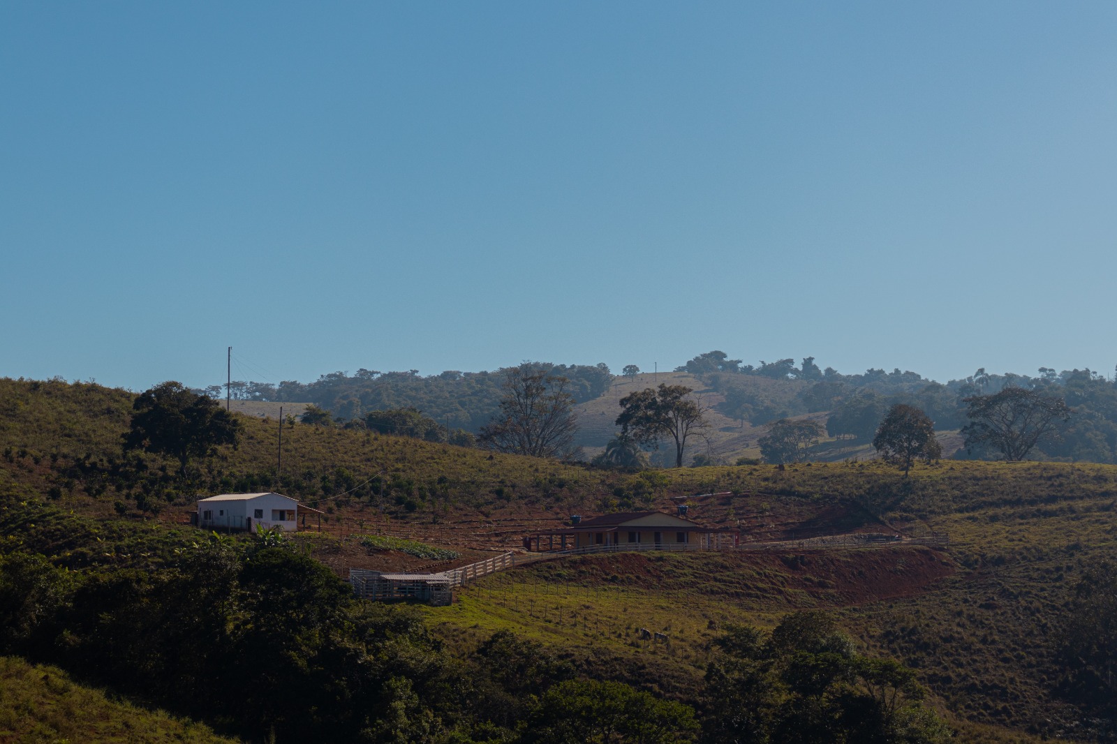 Casinha branca simples no campo com cerca na frente entre montanhas.