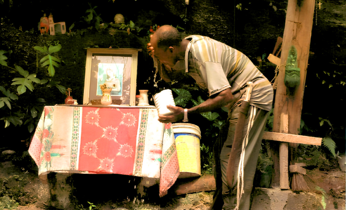 Homem negro lava rosto com água em frente a altar