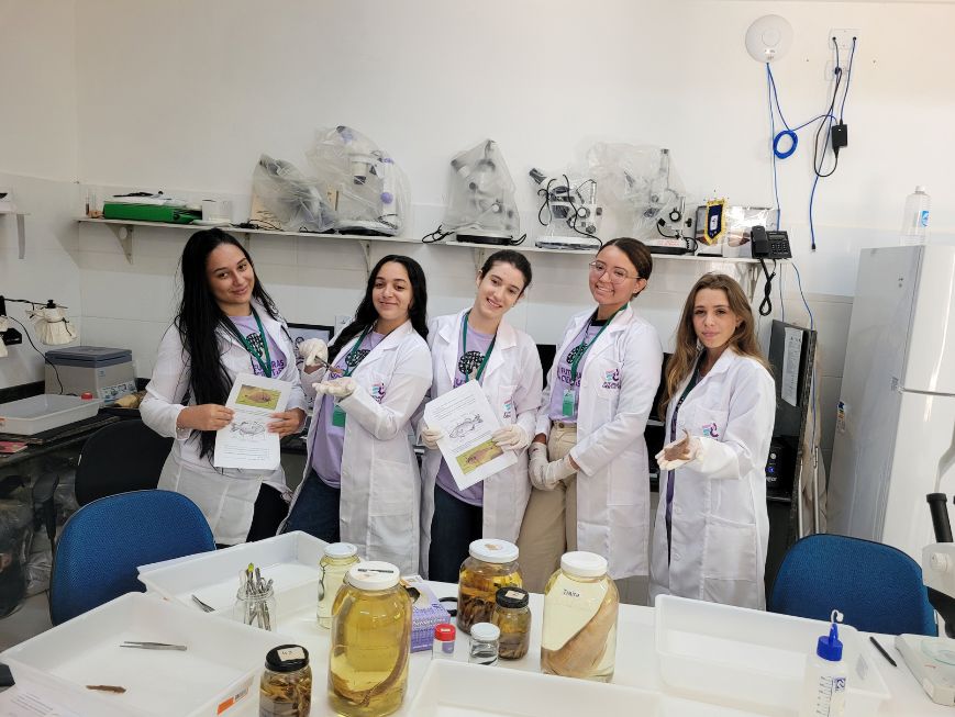 Fotografia de cinco jovens estudantes usando jalecos em um laboratório do Instituto Nacional da Mata Atlântica (INMA).