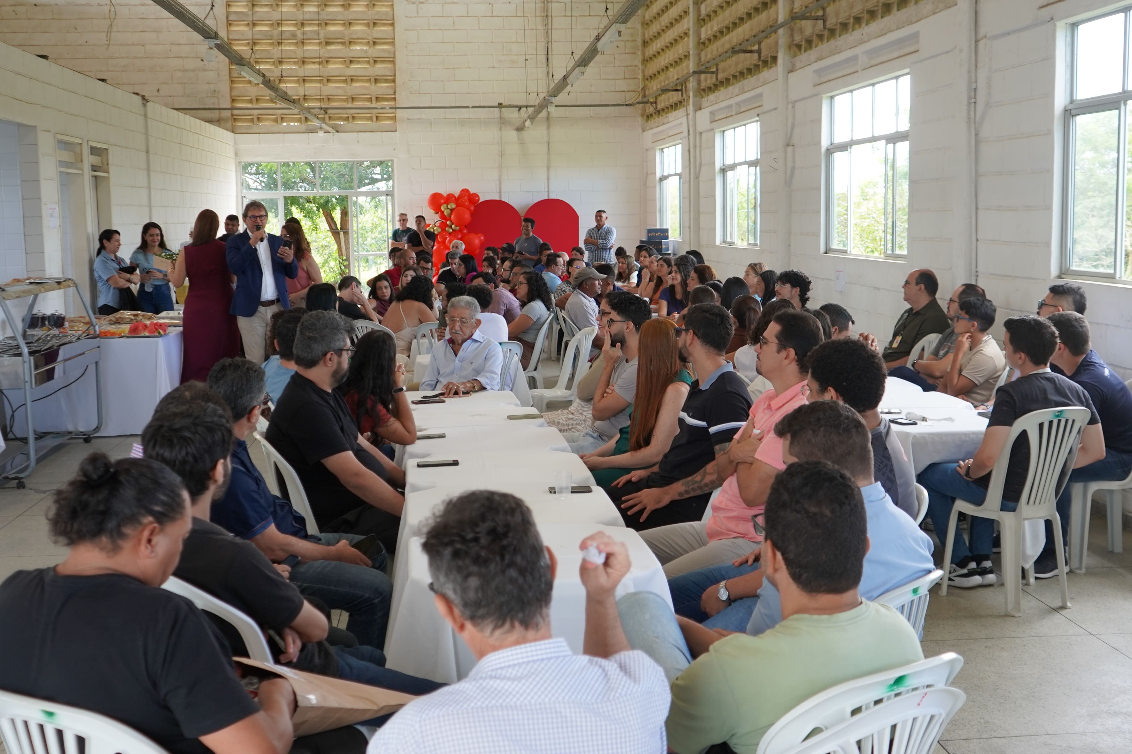 Foto em plano geral. Trabalhadores do INSA reunidos em um salão ouvindo a fala do diretor.