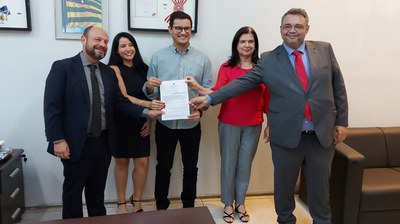 Descrição da imagem: Representantes do INSS e da EMATER seguram documento de cooperação após a assinatura. Foto: Secom/GO.