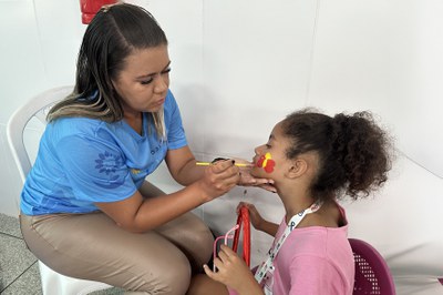 Camila de Sá, voluntária na ação do projeto, realiza pintura de rosto infantil.