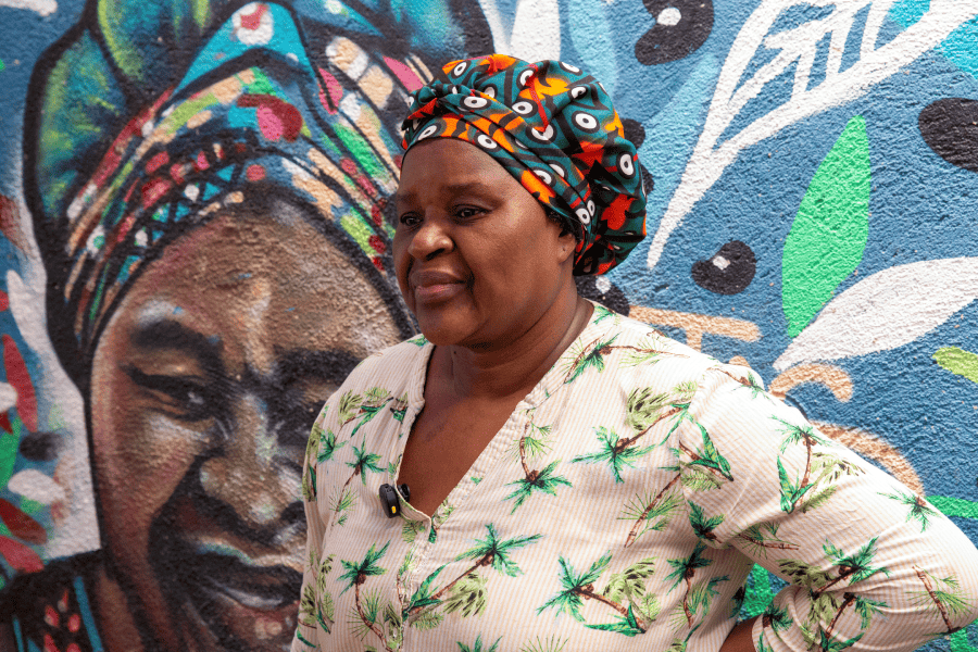 Tia Cida posa em frente a um mural ilustrativo