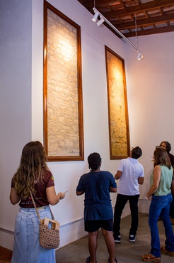 Molduras de janela destacam tijolos de adobe à mostra na parede: valorização e materialidade da história do imóvel.