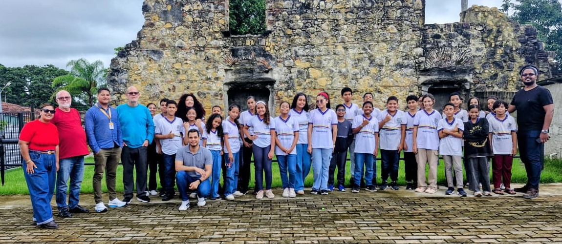 Grupo de crianças posam com equipe do Iphan em frente às ruínas