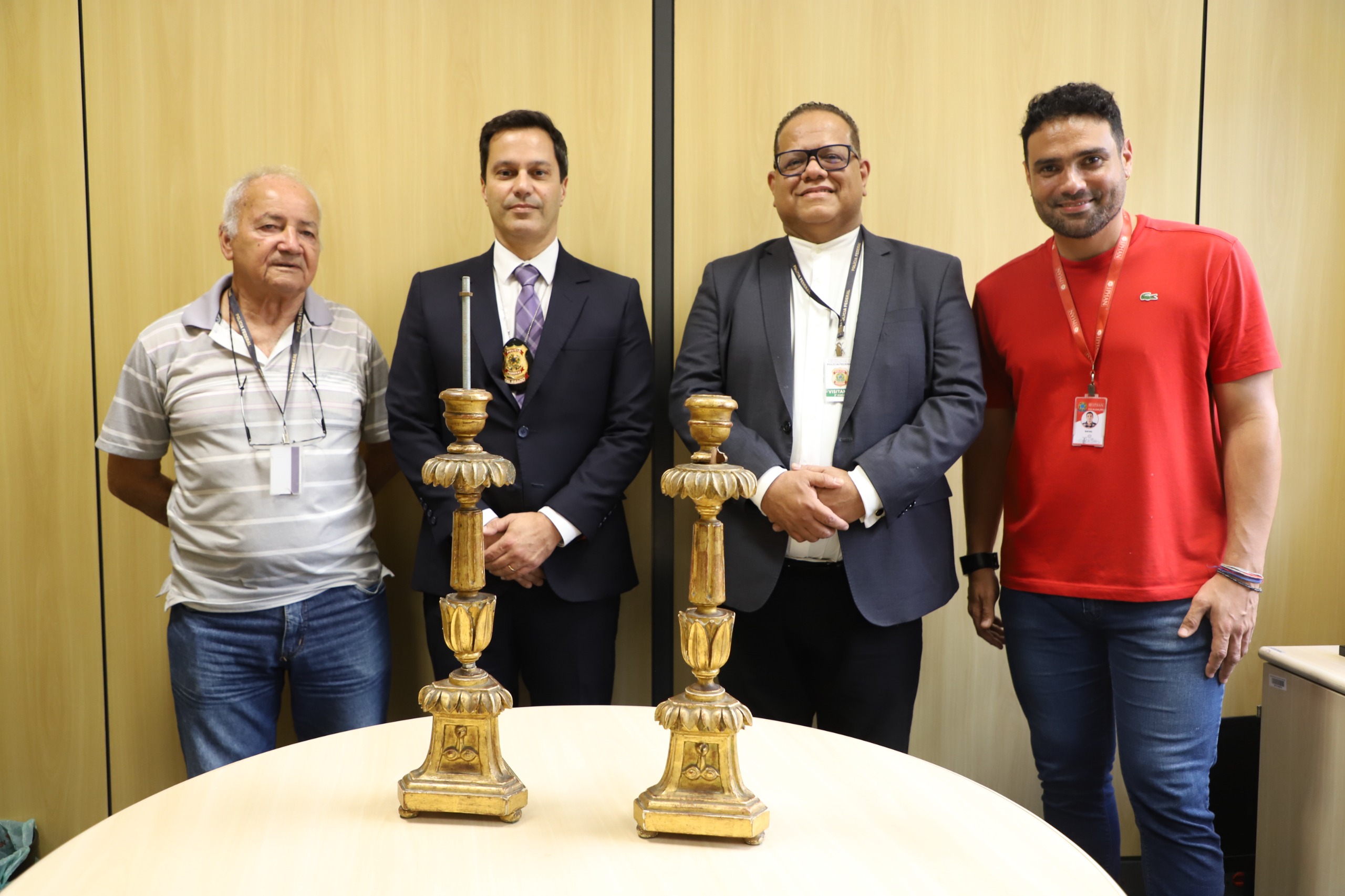 Quatro homens atrás da mesa onde estão os dois castiçais