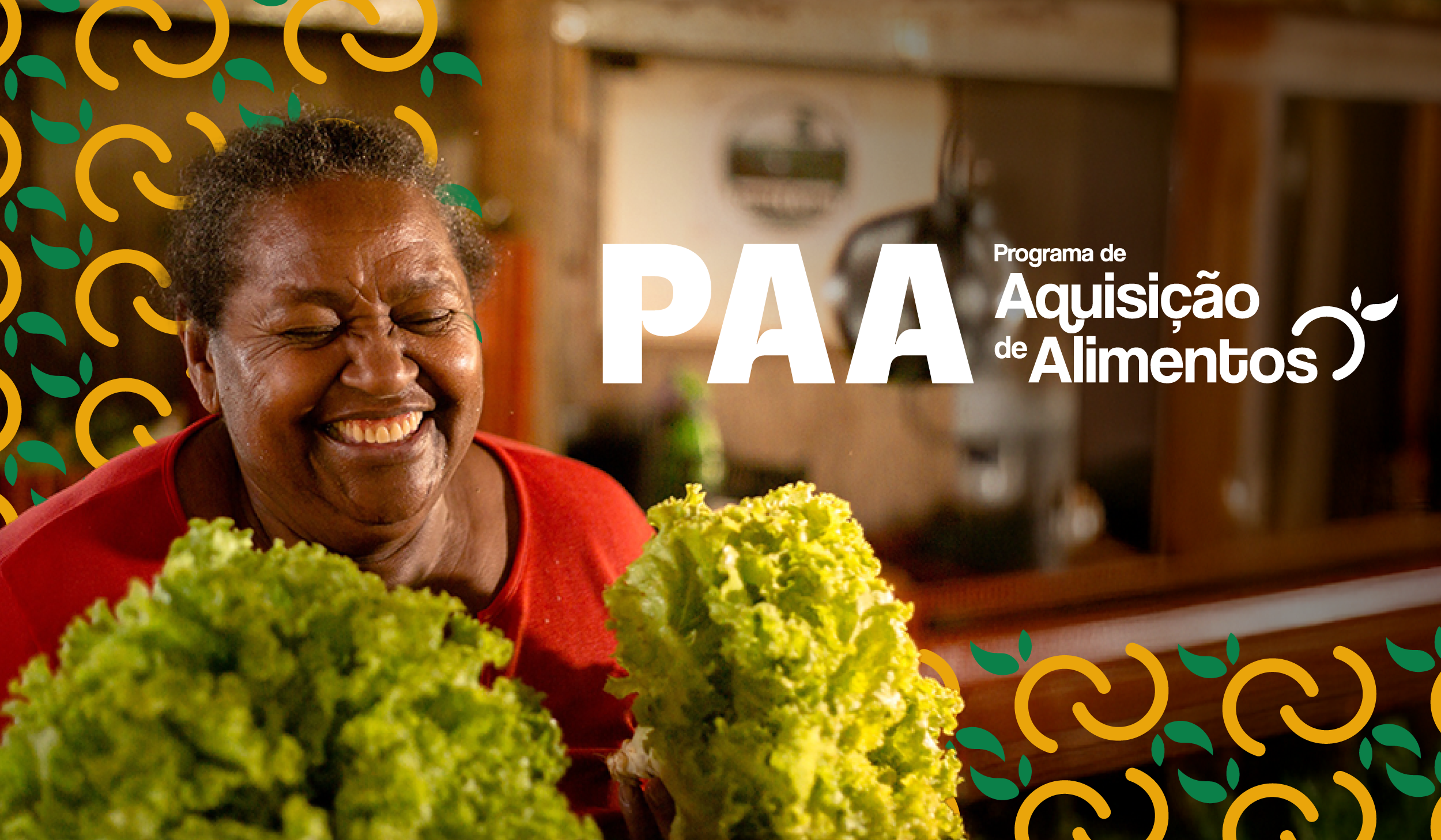 "Mulher sorridente segura dois maços de alface frescos. Ao fundo, elementos gráficos em verde e amarelo decoram a imagem. À direita, aparece o texto ‘PAA – Programa de Aquisição de Alimentos’ em branco."