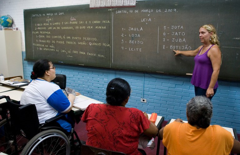 Professora conduz atividade de alfabetização com estudantes da educação de jovens e adultos (EJA) em sala de aula, prática ligada a iniciativas reconhecidas pela Medalha Paulo Freire.